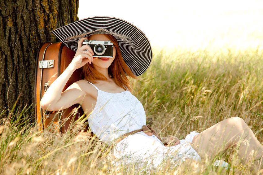 Redhead girl sitting near tree with vintage camera.