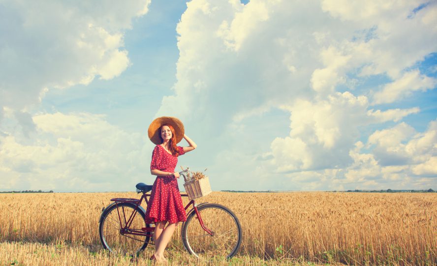Redhead peasant girl with bicycle on wheat field.