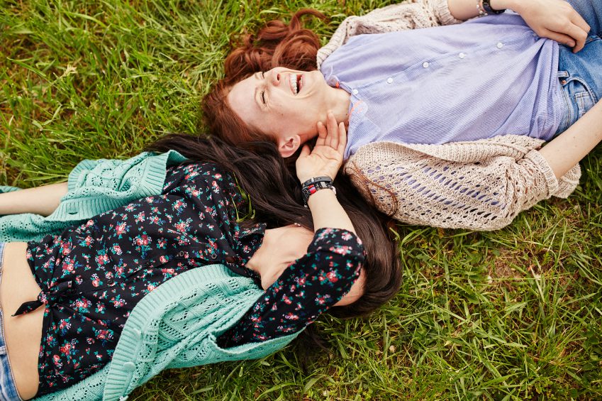 Two cheerful sisters lying on the grass