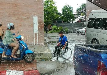 คนพิการจอดรถเข็นกลางสายฝน รอผู้ใช้ จยย. ลงจากทางเท้า ก่อนขึ้นไป